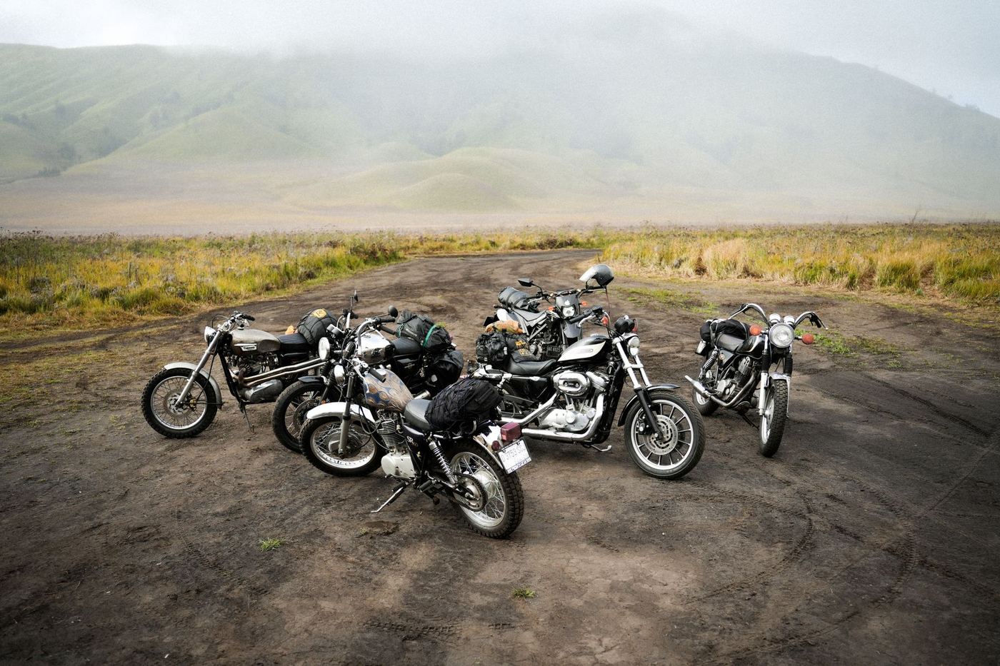 Pięć motocykli zaparkowanych na szutrowym placu, w tle góry we mgle