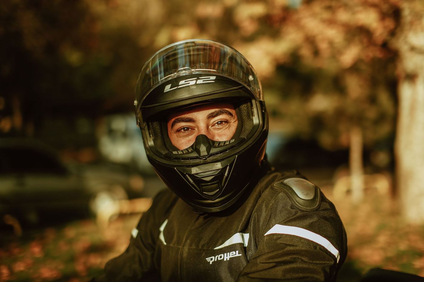 Motocyklista w kasku integralnym i kurtce z odblaskami, jesienne drzewa w tle