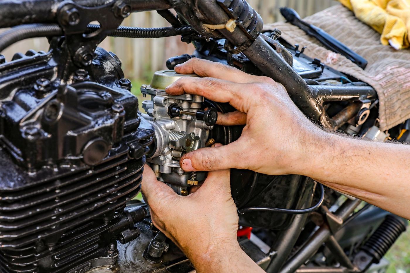 Dłonie mechanika przy gaźniku motocykla, zbliżenie na silnik