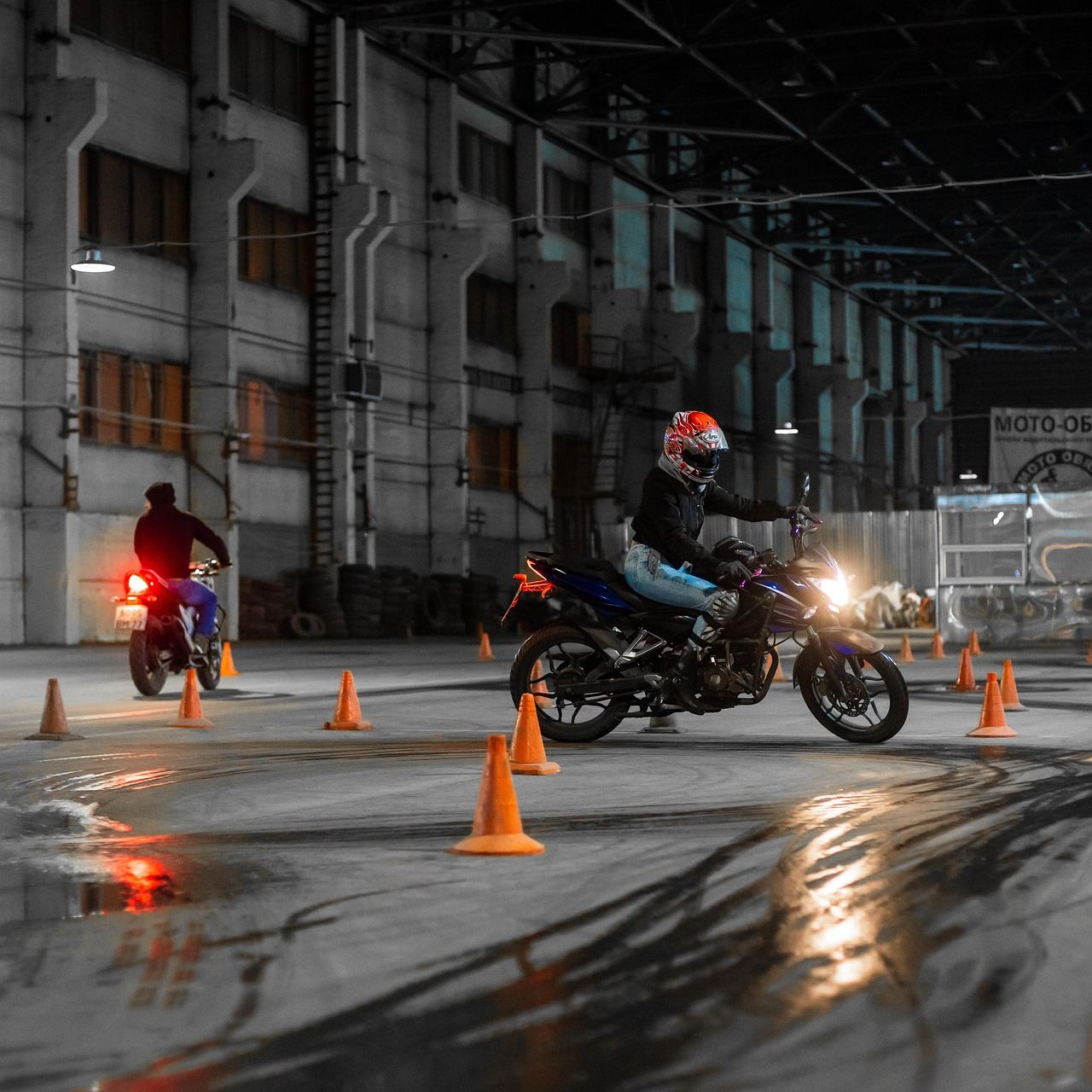 Motocykliści ćwiczą slalom między pachołkami na mokrym placu manewrowym